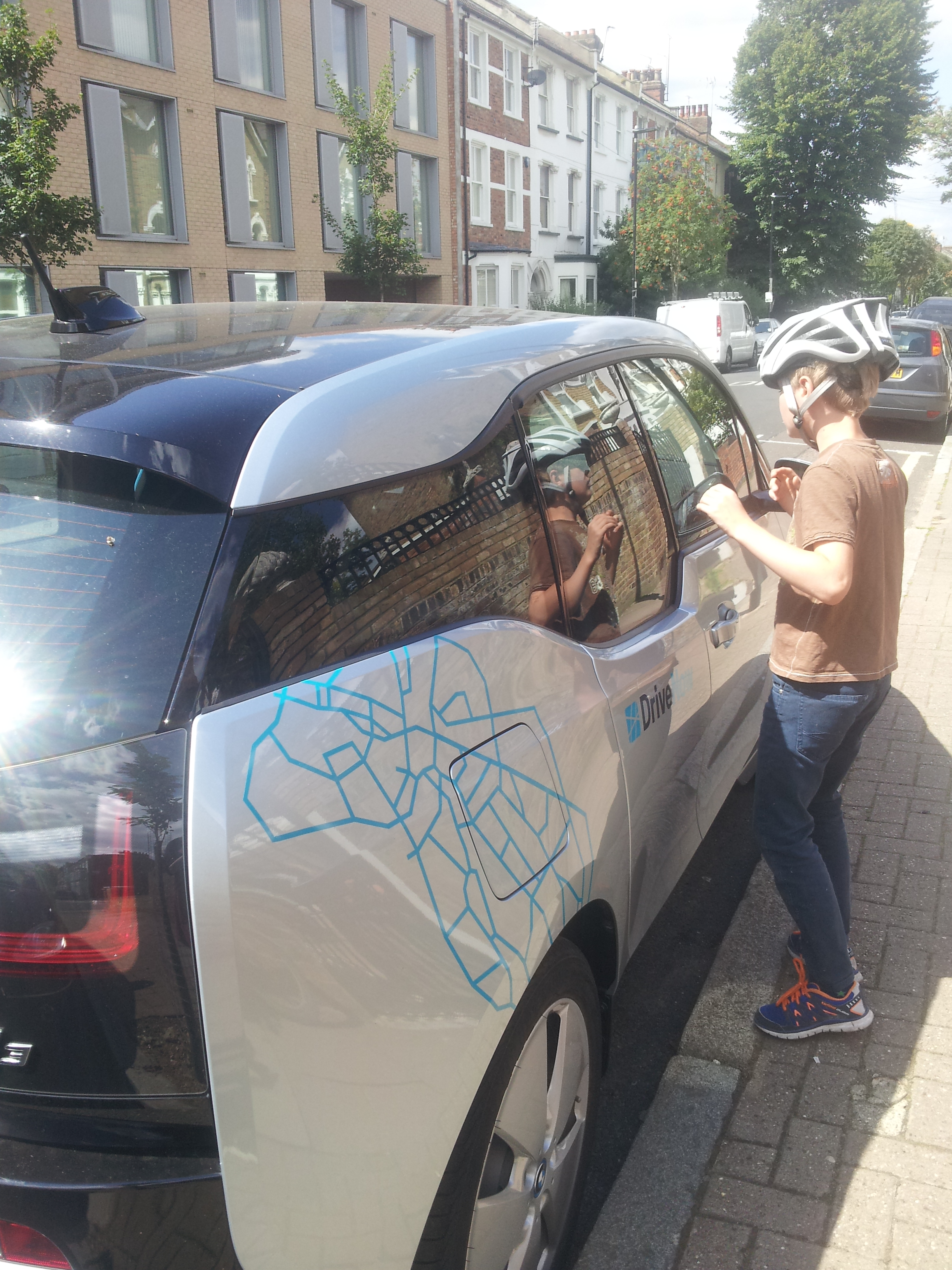 Young cyclist takes a look at a DriveNow vehicle parked outside Arsenal's old Highbury stadium.